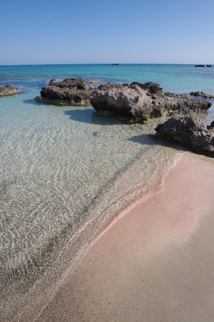 Seichter Strand mit Felsbrocken. Rosa gefärbter Sand am Wasser-Land-Übergang.