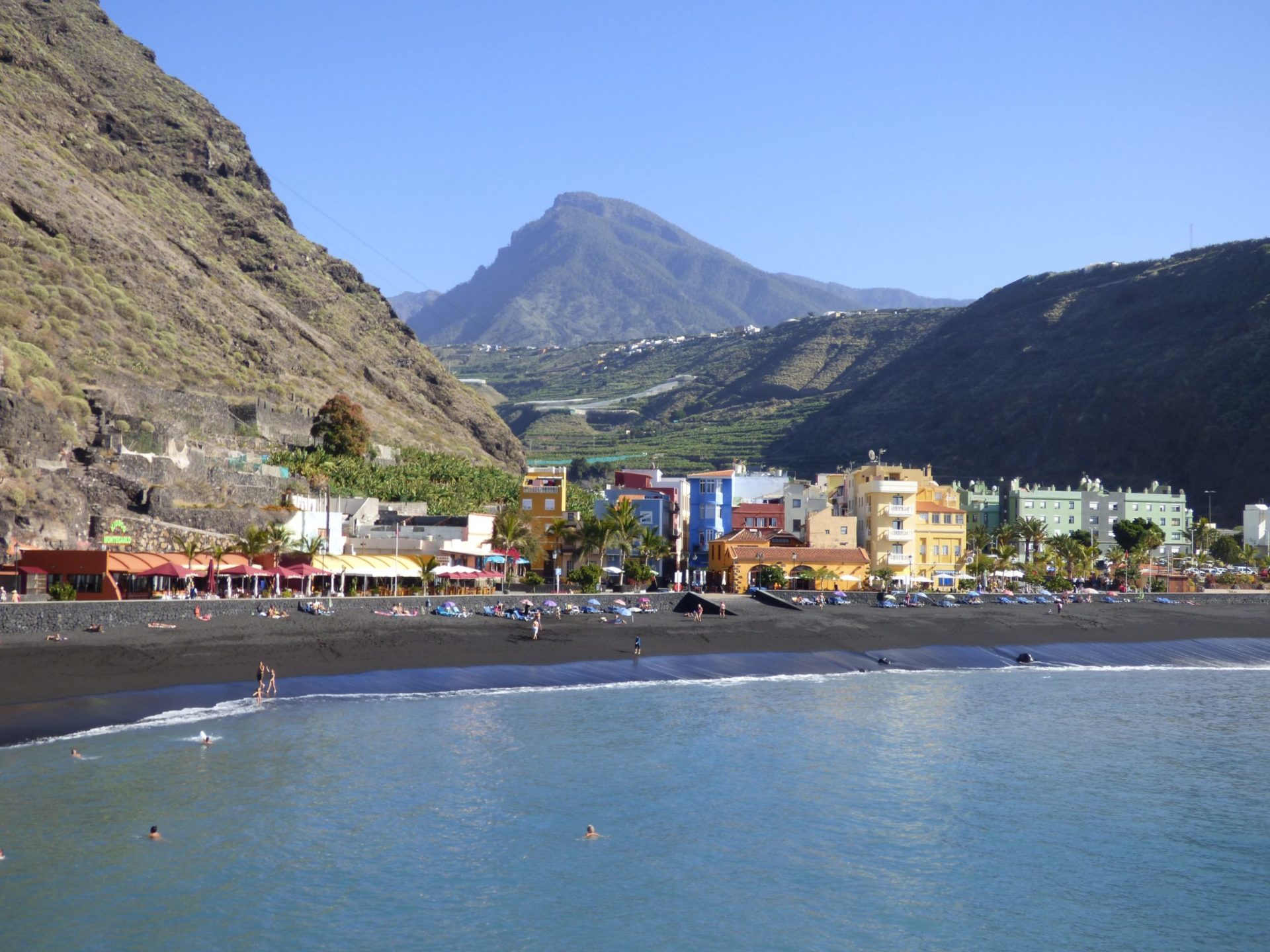 Wassertemperatur La Palma: Badestrand von Puerto de Tazacorte mit bunten Häusern, schwarzem Sand und gebirgigem Hinterland